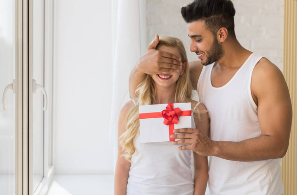 Young Beautiful Couple Stand Near Big Window, Hispanic Man Give Woman Surprise Present Envelope With Ribbon - Fotoğraf, Görsel