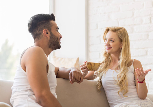 Young Beautiful Couple Sit On Sofa Talking, Hispanic Man Woman Drink Morning Coffee Cup - Zdjęcie, obraz