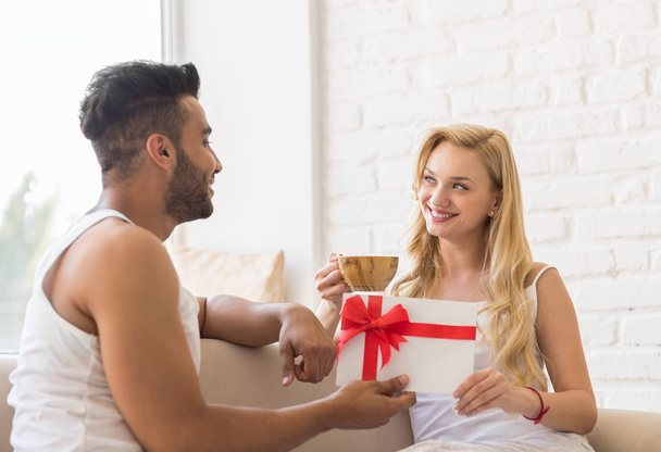 Young Couple Near Window Happy Smile Hispanic Man Woman Hold Present Envelope With Ribbon Lovers In Bedroom - Fotografie, Obrázek