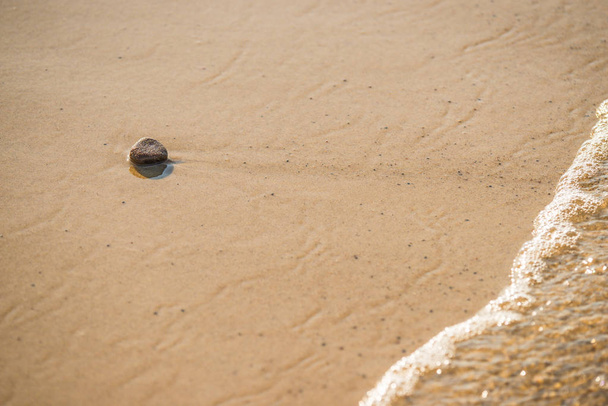 Ein Stein auf einem Sandstrand mit Brandung - Foto, Bild