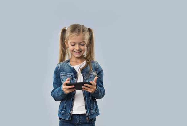 Beautiful Little Girl Using Cell Smart Phone Happy Smiling Wear Jeans Coat Isolated - Foto, afbeelding