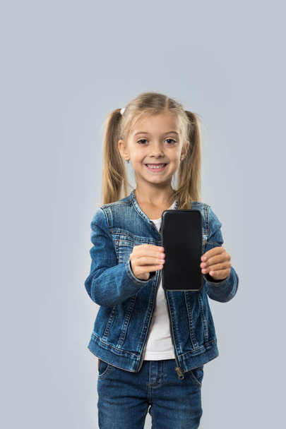 Beautiful Little Girl Hold Cell Smart Phone Empty Screen Happy Smiling Wear Jeans Coat Isolated - Fotó, kép