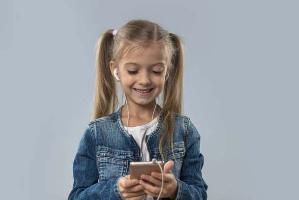 Beautiful Little Girl Using Cell Smart Phone Listen Music Wear Earphones Happy Smiling Isolated - Foto, Bild