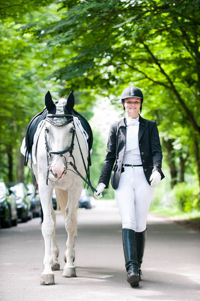 Χαμογελώντας αρκετά εφηβικό κορίτσι κορυφαίο λευκό άλογο στο διαγωνισμό - Φωτογραφία, εικόνα