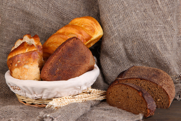 Fresh bread in basket on wooden table on sacking background - Photo, Image
