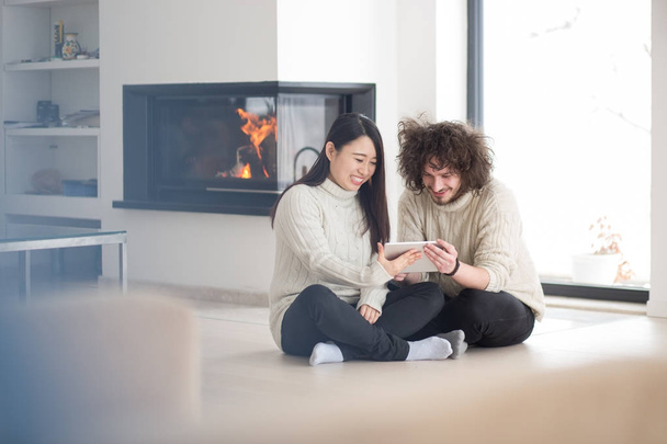 multiethnic couple using tablet computer in front of fireplace - Foto, immagini