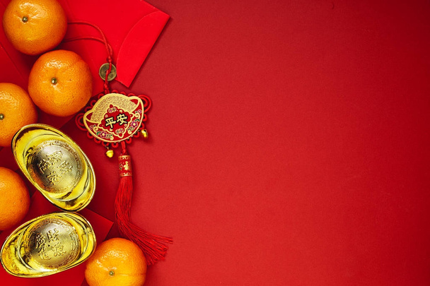 Čínská mince štěstí nebo čínský uzel a čínské zlaté ingoty a tradiční čínský uzel (cizojazyčného textu znamená požehnání) a červené obálky a dekorace s čerstvé pomeranče na červené papírové pozadí - Fotografie, Obrázek