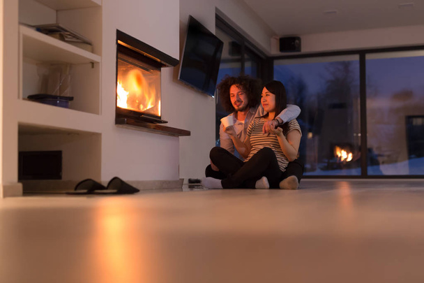happy multiethnic couple sitting in front of fireplace - Fotó, kép
