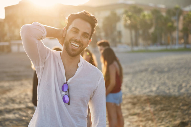 Handsome man on beach holding hand on head smiling - Photo, Image