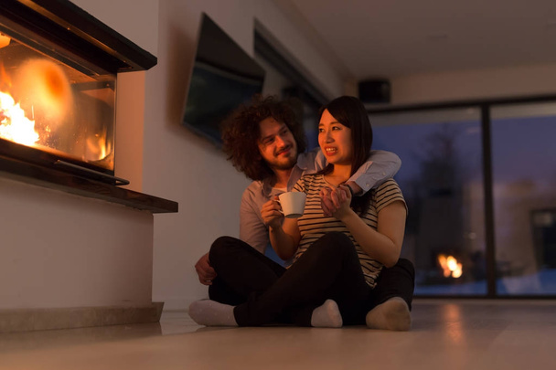 happy multiethnic couple sitting in front of fireplace - Photo, Image