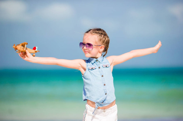 Ευτυχισμένο κοριτσάκι με αεροπλάνο παιχνίδι στα χέρια σε λευκή αμμώδη παραλία - Φωτογραφία, εικόνα