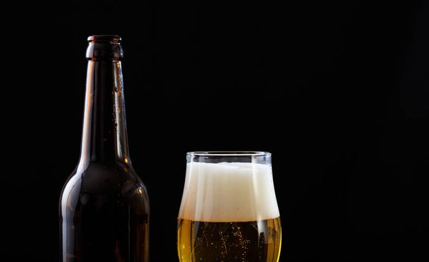 A bottle and a glass of beer closeup, black background - Фото, изображение