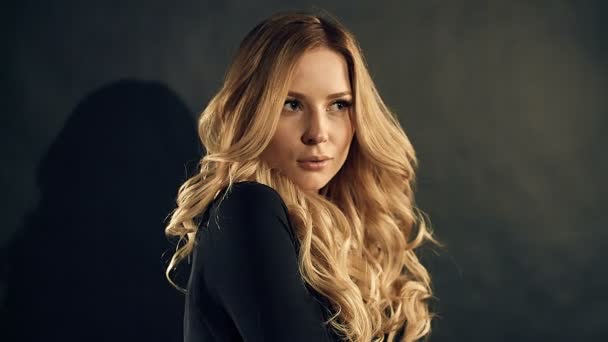 Blondine mit lockigem Haar posiert auf schwarzem Hintergrund im Studio - Filmmaterial, Video