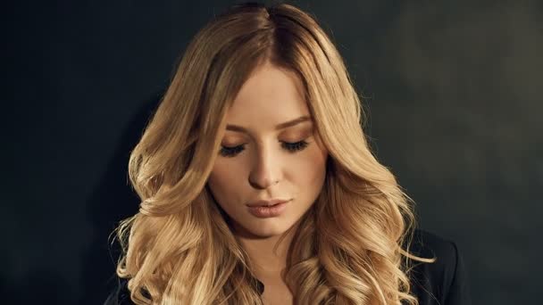 Blondýnka s kudrnatými vlasy zlaté pózuje na černém pozadí v studio - Záběry, video