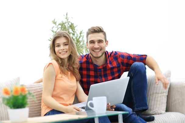 young couple of students uses a laptop sitting on sofa - Foto, afbeelding