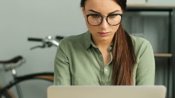 Close up of young atractive woman wearing glasses and working with laptop computer in modern urban office. Woman thinking while looking at the window. - Кадри, відео