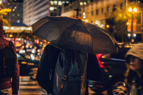 Man met paraplu in de straat op regenachtige nachttijd stad lopen uit het werk - Foto, afbeelding