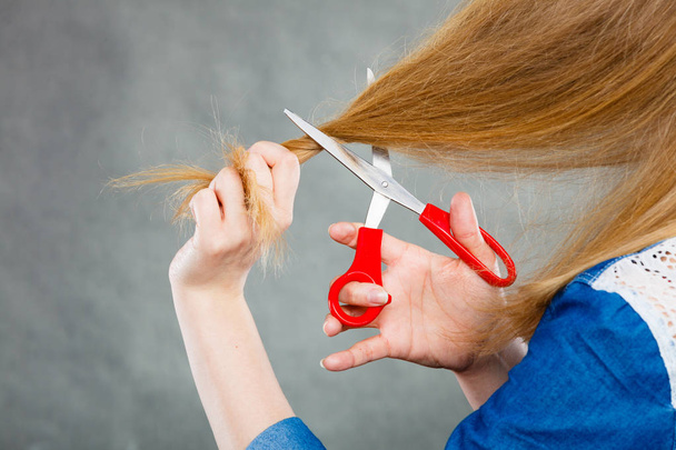 Blonde woman cutting her hair. - Фото, изображение