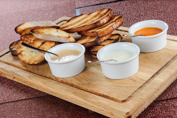 Rebanada de pan tostado empanado con queso y sésamo deslizado en una salsa sobre una tabla de madera
 - Foto, imagen