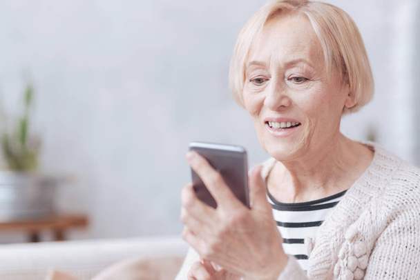 Pretty excited elderly woman texting on phone - Foto, Bild