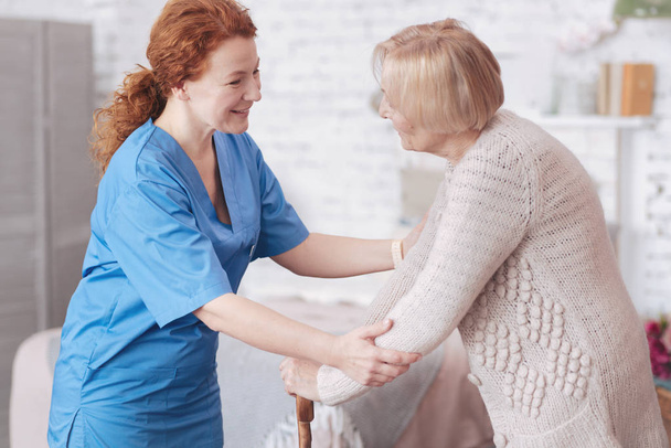 Positive caregiver having pleasant conversation with retired lady - Фото, изображение