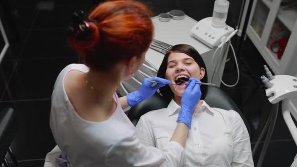 Γυναίκα γιατρός εξετάζει έναν ασθενή σε ένα λευκό πουκάμισο σε ένα άσπρο αποστειρωμένο γραφείο στο μπλε γάντια. Διεξάγει την προφορική εξέταση. - Πλάνα, βίντεο