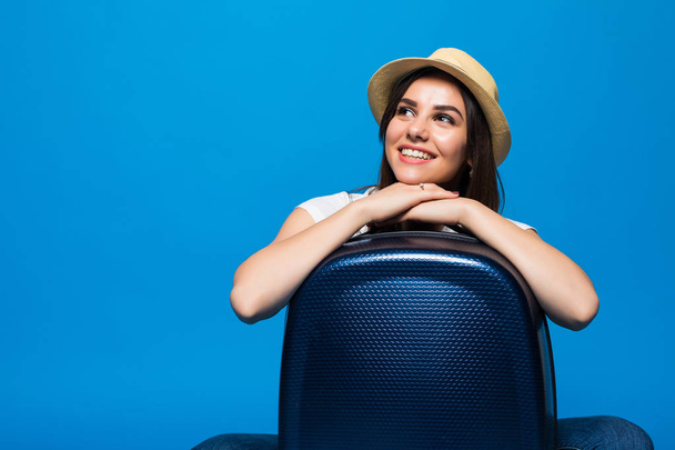 Young Woman sitting near a suitcase baggage on a blue background. - Фото, зображення