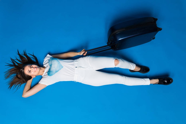 青の背景に床に位置しながら旅の女の子の夢。孤立した背景に横たわっている荷物を持つ女性 - 写真・画像