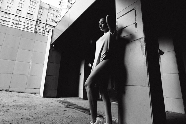 young woman with bare legs dressed in white sneakers and a long T-shirt, against the backdrop of cityscapes - 写真・画像