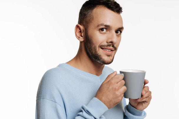 Dark-haired bristled man holding a cup of coffee - Zdjęcie, obraz