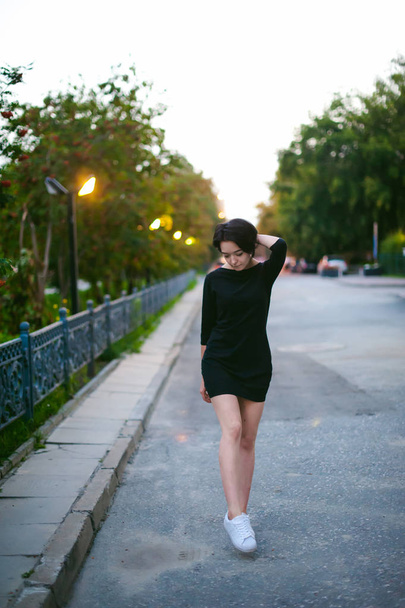 young woman with beautiful feet dressed in white sneakers and black dress, against a backdrop of urban landscapes. Street fashion. dark style - Φωτογραφία, εικόνα