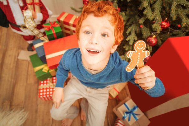 Excited ginger child looking into camera while holding gingerbread man - Foto, immagini