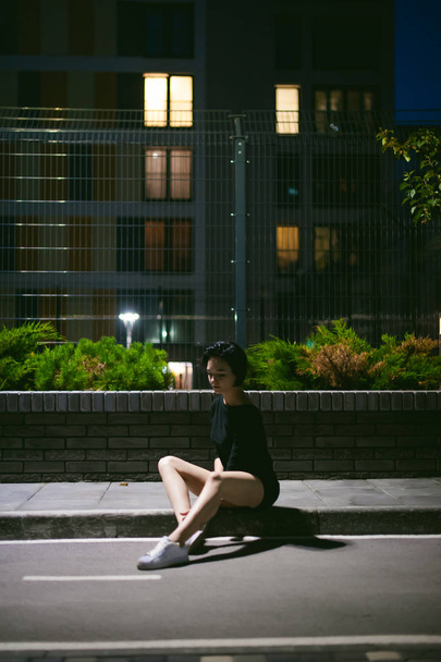 young woman with beautiful feet dressed in white sneakers and black dress, against a backdrop of urban landscapes - 写真・画像