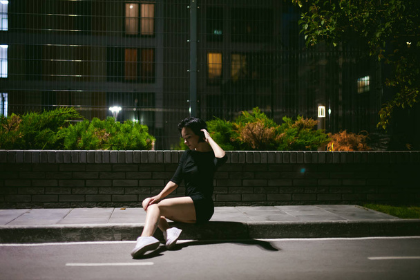 young woman with beautiful feet dressed in white sneakers and black dress, against a backdrop of urban landscapes - Foto, imagen