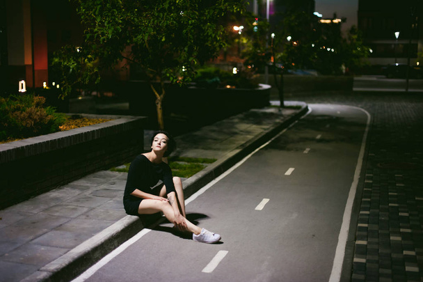 young woman with beautiful feet dressed in white sneakers and black dress, against a backdrop of urban landscapes - Foto, Imagen