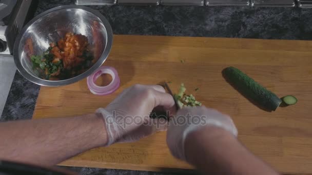 Professional chef in gloves slicing cucumber on wood board at commercial kitchen - Кадри, відео