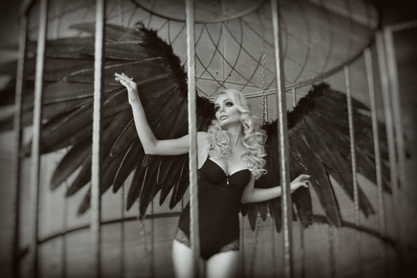 blond woman with black wings in a cage. Angel, mysticism - Photo, Image