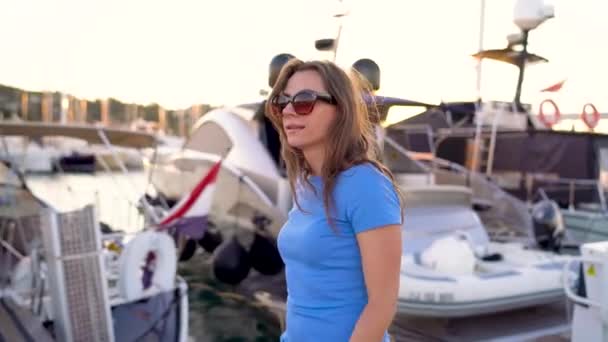 Woman in sunglasses walking along the dock with a lot of yachts and boats at sunset, close up. Slow motion - Filmati, video