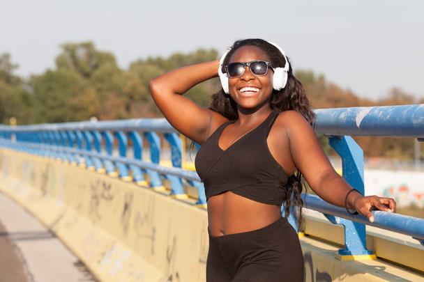 Young African woman wearing sportswear and listening to music on the street - Fotó, kép