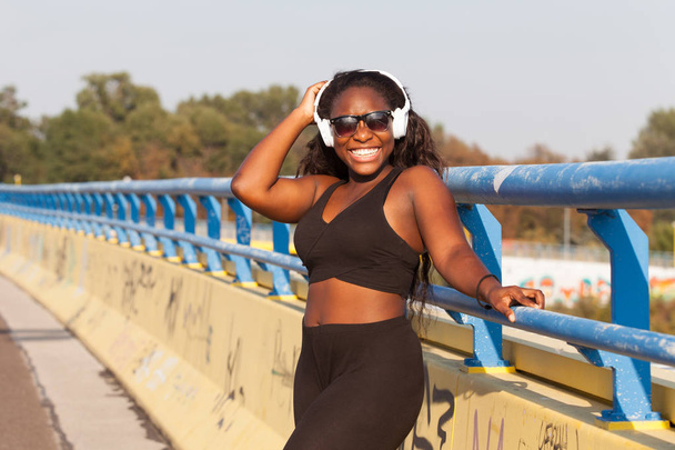 Fiatal afrikai nő visel sportruházat és hallgató-hoz zene-az utcán - Fotó, kép