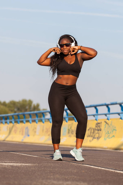 Fiatal afrikai nő visel sportruházat és hallgató-hoz zene-az utcán - Fotó, kép
