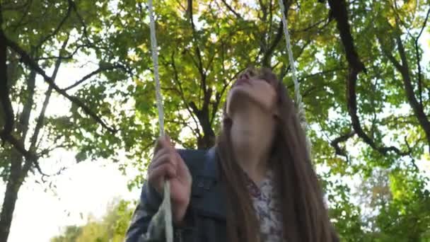 A girl is riding on a swing in the park. The camera moves from bottom to top. - Footage, Video