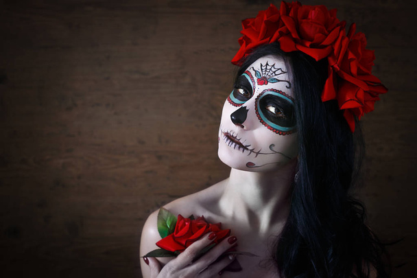 Dag van de doden. Halloween. Jonge vrouw in dag van de dode masker schedel gezicht kunst en rose. Donkere achtergrond. - Foto, afbeelding
