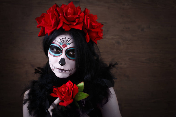 Le jour des morts. Halloween. Jeune femme dans le jour de la mort masque crâne visage art et rose. Fond sombre
. - Photo, image