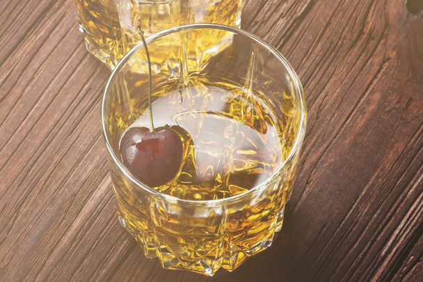 Cocktail from whisky with cherry in two glasses on a wooden back - Фото, зображення