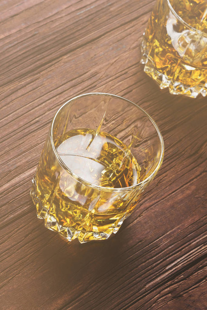 Whisky with ice in two glasses on a wooden background. Toned - Фото, зображення