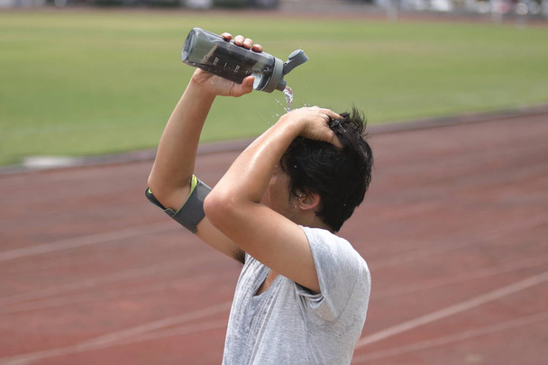 Saludable joven corredor asiático vertiendo agua con botella de agua en su cara después de correr en pista en el estadio
. - Foto, Imagen