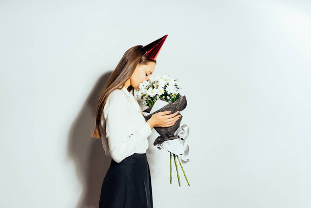 young happy girl celebrating something, wearing a cap, holding a big bouquet of white flowers - Photo, Image