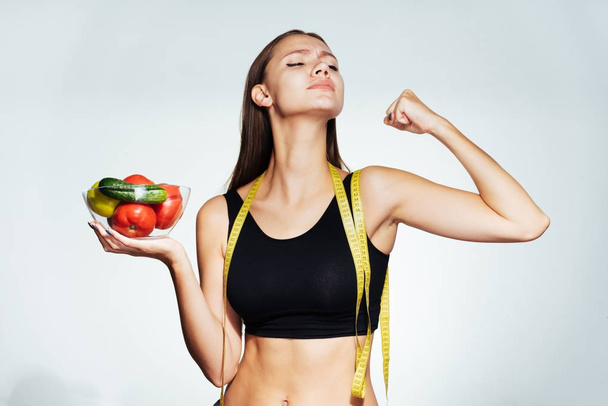 a young athletic girl in a black top keeps track of her figure, holds a plate with useful vegetables and fruits in her hands - Photo, Image
