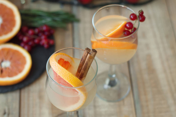 Citronnade au pamplemousse, bâtonnets de cannelle et groseille rouge servis dans des verres à vin sur une table en bois
 - Photo, image